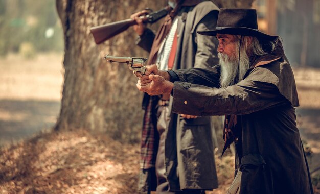 Photo men holding gun wearing hat standing at forest