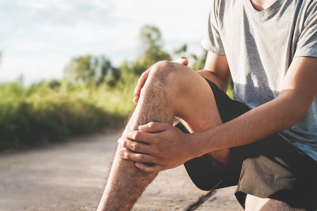 men injured from exercise, use his hands to hold his knees at the park