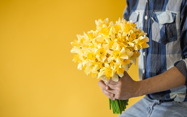 Men in jeans and a shirt holding a large bouquet of daffodils.