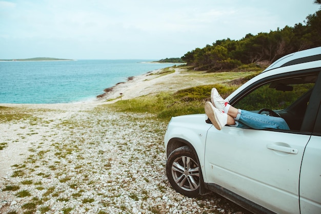 Men legs stick out from car parked at sea beach summer vacation