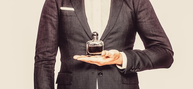 Men perfumes Fashion cologne bottle Man in formal suit bottle of perfume closeup Man holding up bottle of perfume Men perfume in the hand on suit background Fragrance smell