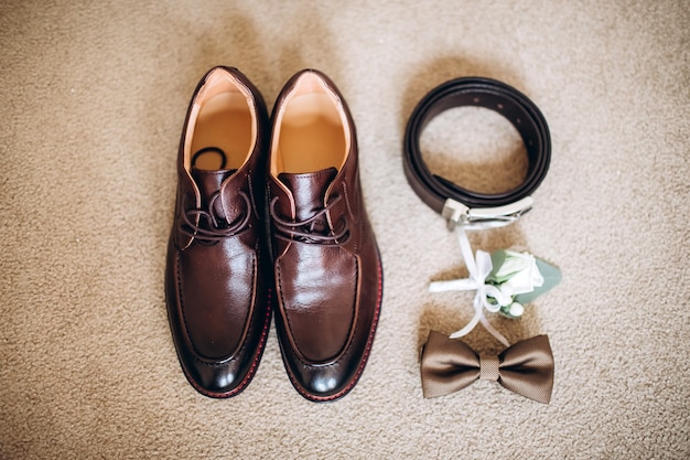 Photo men's accessories, leather belt, perfume, bow tie, groom's golden rings, watches and brides on a white table. businessman clothing detail concept