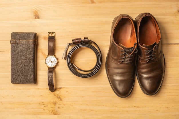 Men's accessories with brown leather wallet, belt, shoes and watch on wooden surface