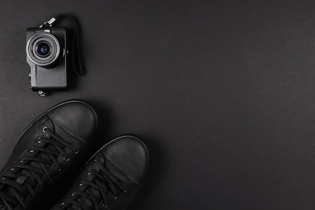 Men's black leather shoes and a black camera on a black background