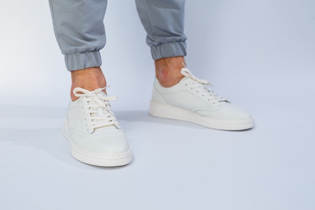 Men's feet in white everyday sneakers made of natural leather on lacing. High quality photo