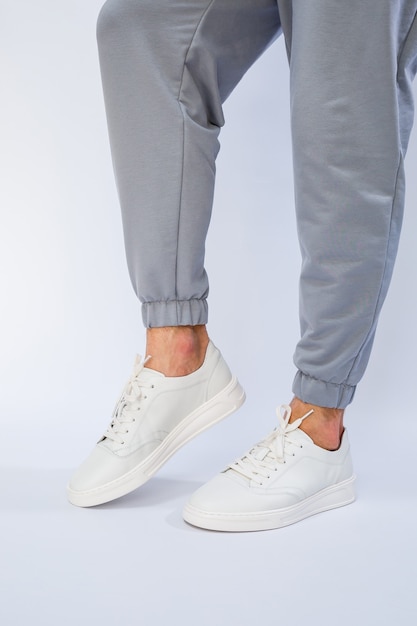 Men's feet in white everyday sneakers made of natural leather on lacing.