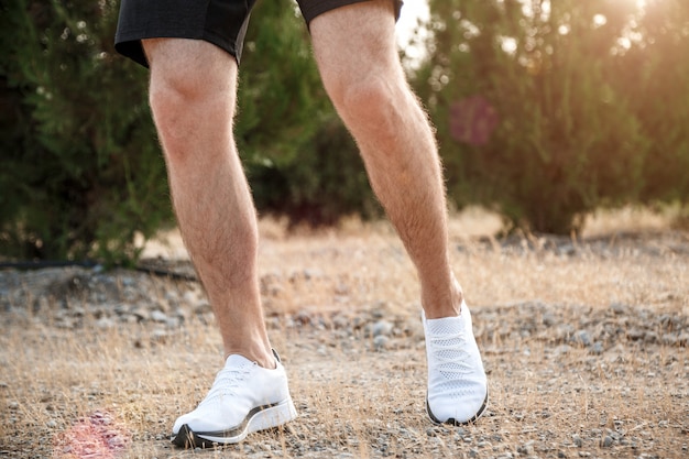 Men's feet in white sneakers running over rough terrain. Cross country running with focus on runner's legs.