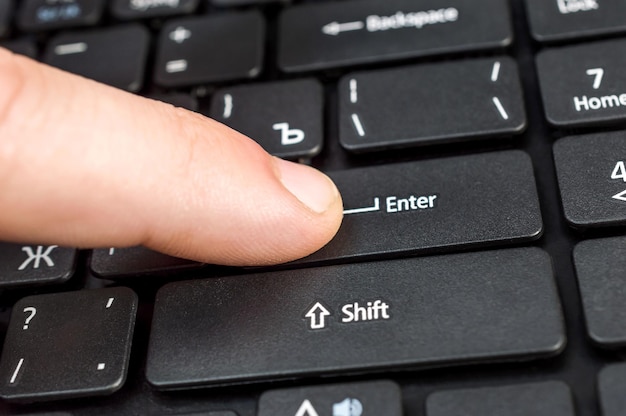 Men's finger pushing on key Enter on the laptop keyboard Close up