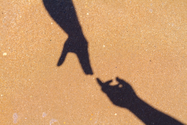 men's hand reaches for women's hand shadow on sand background