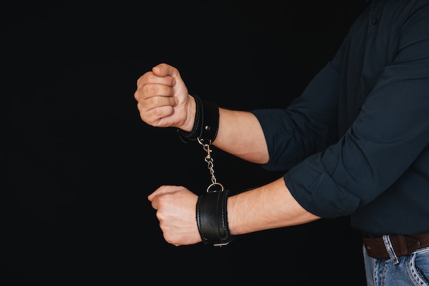 Men's hands chained in leather handcuffs on black 