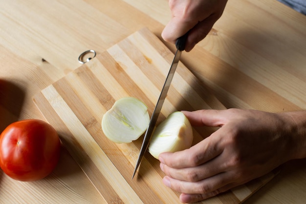 Men's hands cut onions on a wooden board