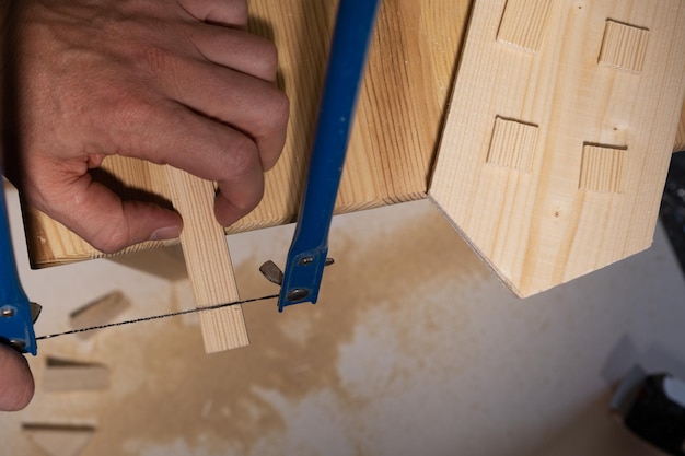 Men's hands cut a rail with a hand jigsaw to make a wooden house