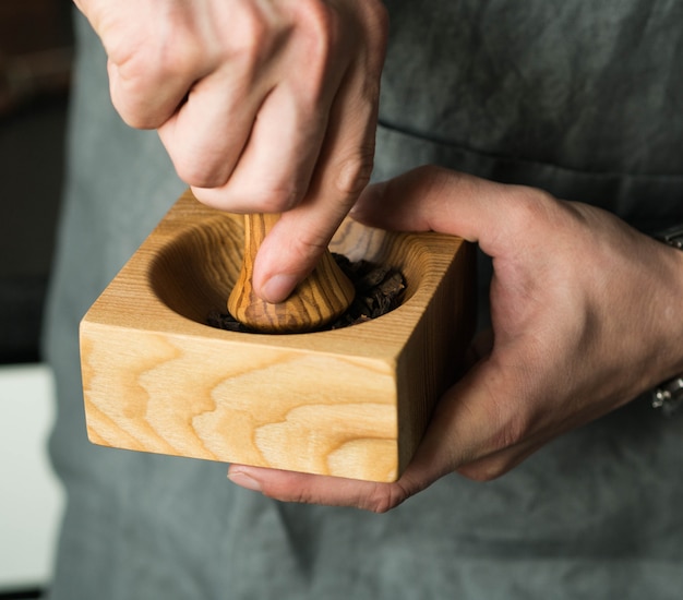 Men's hands grind spices in a wooden mortar