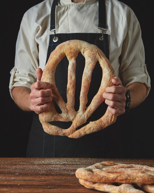 Men's hands holding fresh fougas bread on the black background of a wooden table