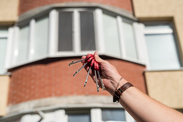 Men's hands holding a key with a keychain in the shape of a house on the background of a cool house The interior of a modern bright lobby Mortgage concept Real estate moving or renting real estate