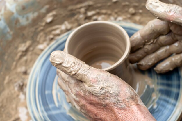 Men's hands making a clay mug on a potter's wheel