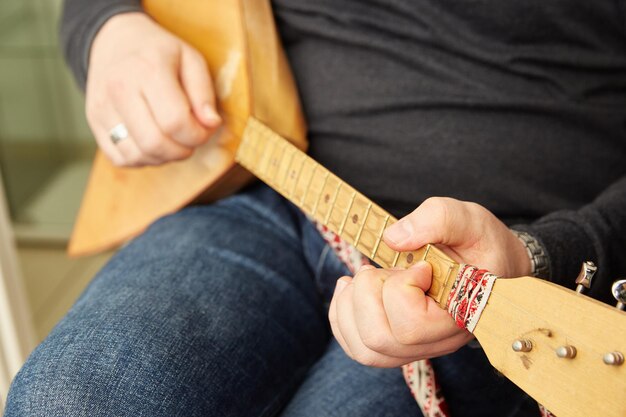 Le mani degli uomini suonano la balalaika, uno strumento musicale a pizzico a corde popolare russo con un corpo a forma triangolare con tre corde