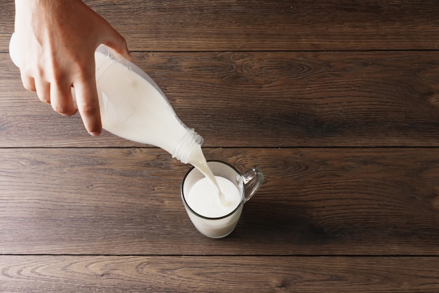 Le mani degli uomini versano il latte da una bottiglia in un bicchiere