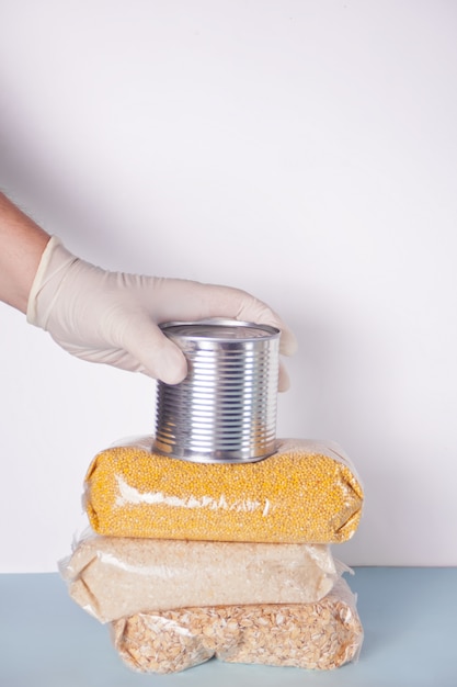 Men's hands with rubber gloves gives tin can with food. Food donation. Food delivery during an epidemic. Contactless product delivery.