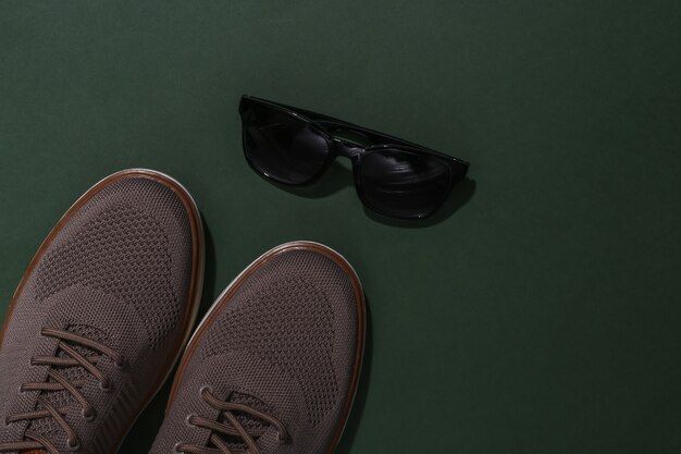 Men's shoes and sunglasses on green background. Top view