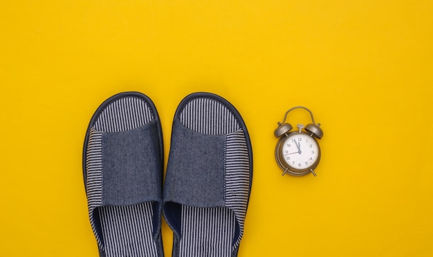 Men's sleeping room slippers and alarm clock on a yellow background. Time to sleep. 