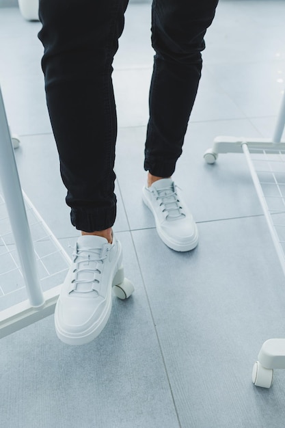 Men's in white leather casual laceup sneakers and black trousers against a gray tile background