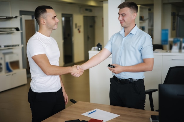 Men shake hands after successful sale in car showroom