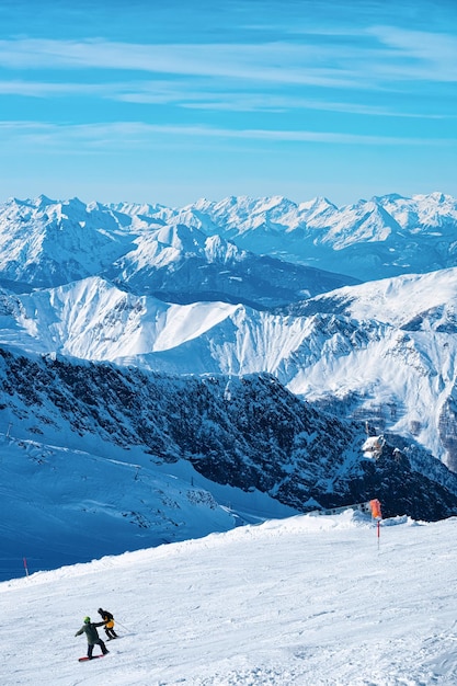 남자 스키어와 스노보더는 오스트리아의 마이어호펜(Mayrhofen)에 있는 티롤(Tyrol)의 힌터툭스(Hintertux) 빙하에서 겨울 알프스입니다. 알파인 산의 Hintertuxer Gletscher에서 스키와 스노보드를 타는 사람들. 햇살이 비추는.