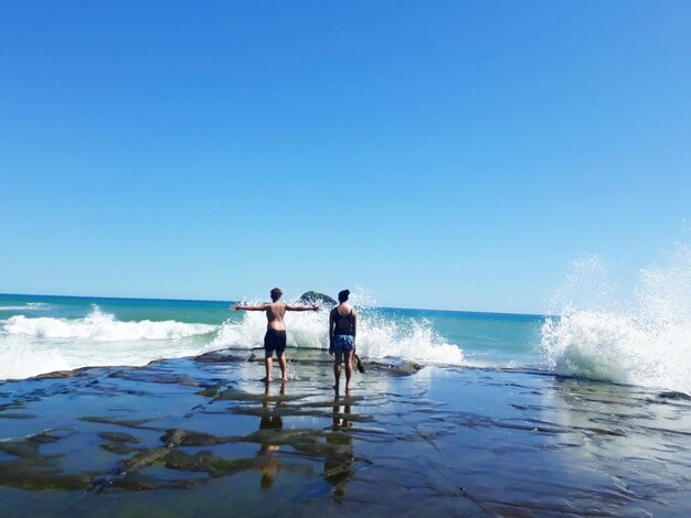 Men standing on beach against clear blue sky