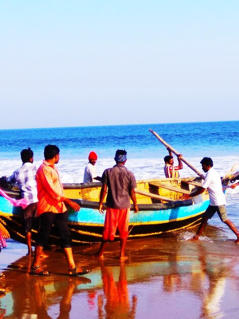 Men standing on boat moored in sea against clear sky