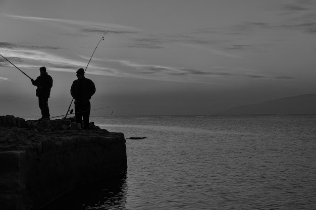 写真 湖で釣りをしている男性が岩の上に立っています