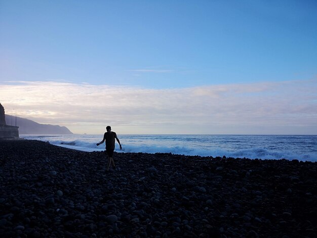 Men standing on rock at beach against sky