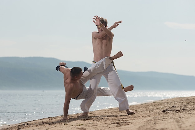 Men train capoeira on the beach - concept about people, lifestyle and sport.