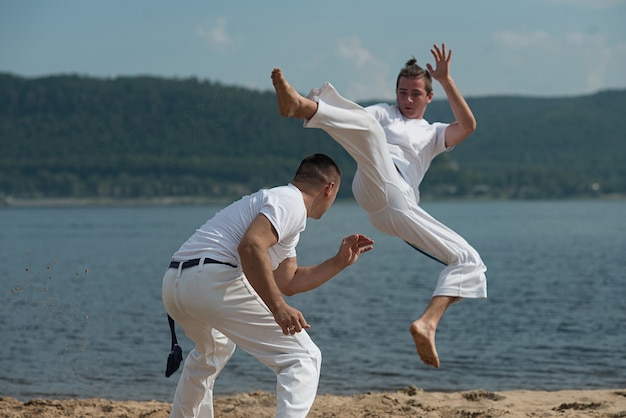 Men train capoeira on the beach 