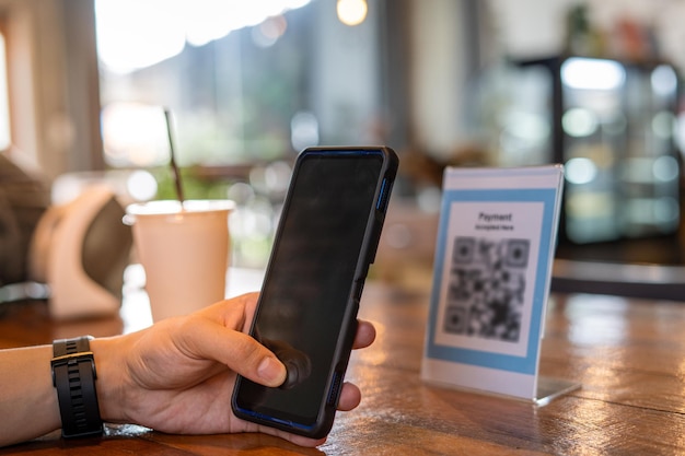 Men use phones to scan a qr code to select a menu or scan to
receive a discount or pay for food and drink inside a cafe using
the phone to transfer money or pay online without cash concept