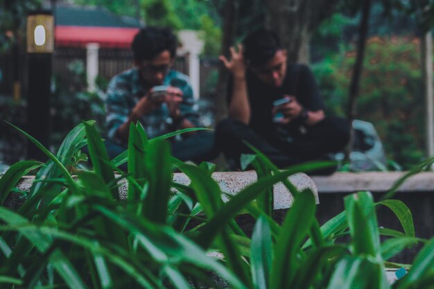 Photo men using phone while sitting against tree trunk