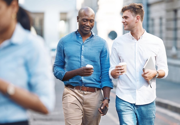 Photo men walk and street with takeaway coffee while talk smile and relax at lunch break black man colleague and diversity in city at tea time walking to office or workplace in discussion or talking