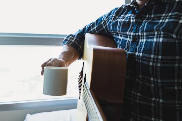 Men wearing a plaid shirt holding a coffee mug after playing the guitar