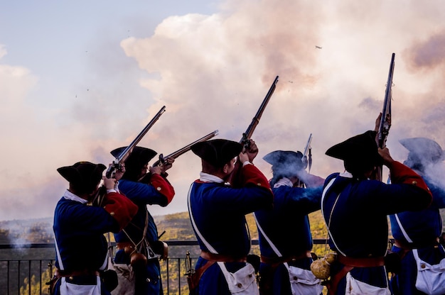 men wearing traditional clothing while shooting riffles against sky