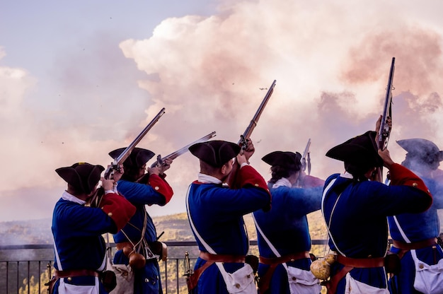men wearing traditional clothing while shooting riffles against sky