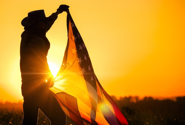 Фото Мужчины в западной одежде празднуют день независимости, размахивая большим американским флагом во время живописного заката висты соединенные штаты америки патриот в ковбойской шляпе