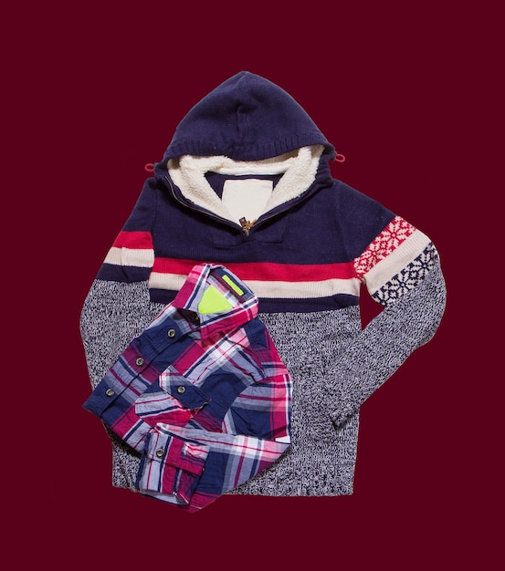 Men winter clothes folded. Jacket with hood and shirt on dark red background