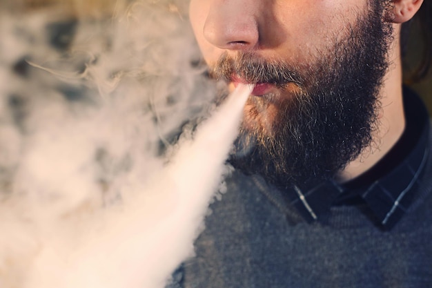 Men with beard vaping and releases a cloud of vapor closeup