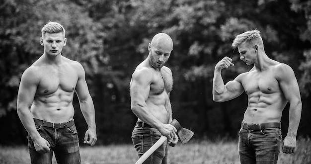 Men with muscular torso Wild masculinity Brotherhood concept Strength and perseverance Strong men nature background Inspiring training harder Group muscular men with axe Athletic man use ax