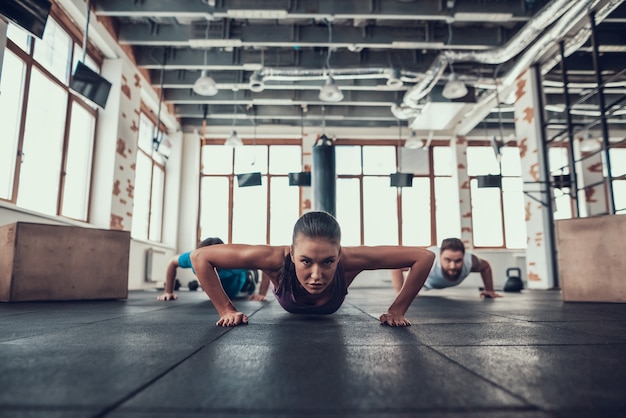 Foto gli uomini e la donna che fanno push ups nella palestra luminosa.