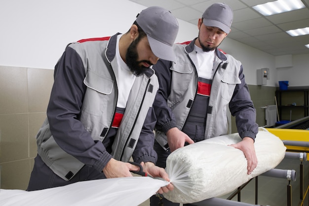 Men workers packing carpet in a plastic bag after cleaning it in automatic washing machine and dryer in the Laundry service