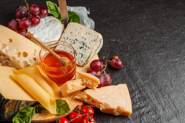 Meng kaas op een donkere achtergrond op een houten bord met druiven, honing, noten, tomaten en basilicum. Bovenaanzicht