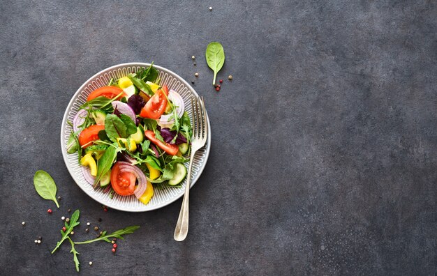 Meng salade met tomaten, uien en olijfolie in een bord op een zwarte betonnen achtergrond.