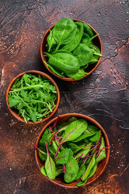 Meng slablaadjes, rucola, spinazie en snijbiet in houten kommen. Donkere achtergrond. Bovenaanzicht.