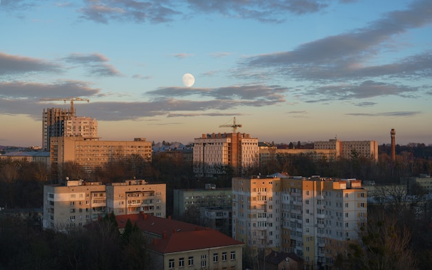 Mening van woningbouw bij de zonsondergang met bewolkte hemel. De maan gezien tussen gebouwen en bouwplaatsen bij zonsondergang in de stad Lviv in Oekraïne.